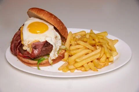 A hamburger with an egg on top and a side of french fries Stock Photos