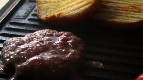 Hamburger in a grill being cooked . The is also two pieces of bread. Steady shot Stock Footage 328483317