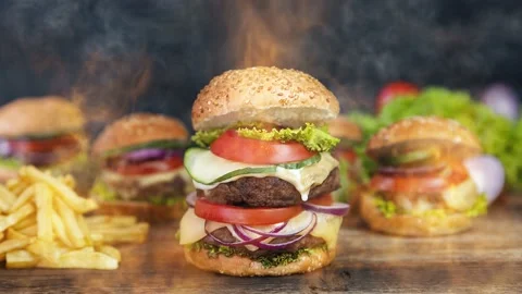 Hamburger served on a rustic wooden surface surrounded by smoke and burning fire Stock Footage 135438980