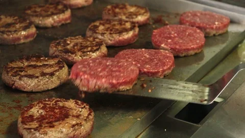 Hamburgers being flipped on a hot griddle with a spatula Stock Footage