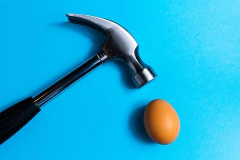 Hammer is hitting on an egg with blue background. minimal idea creative concept. Stock Photos