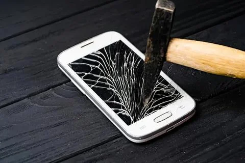Hammer hitting smartphone with broken screen on wooden table Stock Photos