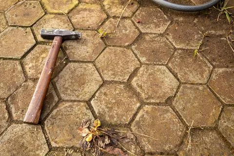Hammer lying on hexagonal paving stone with a garden hose in the background Stock Photos