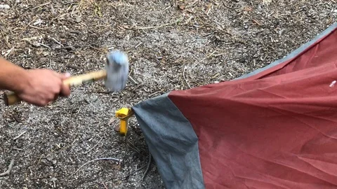 Hammering a long yellow stake through the strap on the tent at the campground Stock Footage 92394845