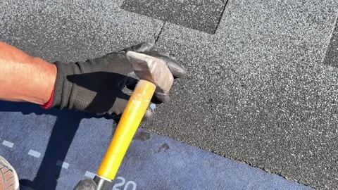 Hammering roofing nails into bitumen shingles during roof installation Stock Footage 346845812