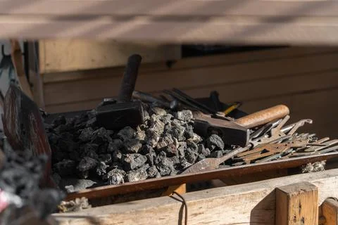 Hammers and blacksmith tools lie on black coal with metal blanks for forging Stock Photos