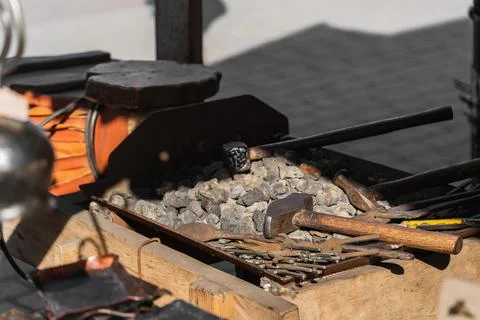 Hammers and blacksmith tools lie on black coal with metal blanks for forging Stock Photos