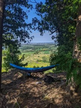 A Hammock  Rests on a Cliff Edge Overlooking Forested Valley &amp; Farm Fields Foto stock