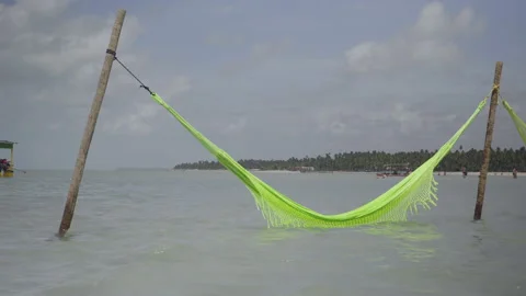 Hammock supported by rustic sticks in shallow water far from the beach Video stock 232804933