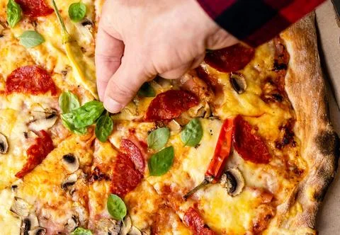 Hand adding basil leaf to freshly baked pizza Stock Photos