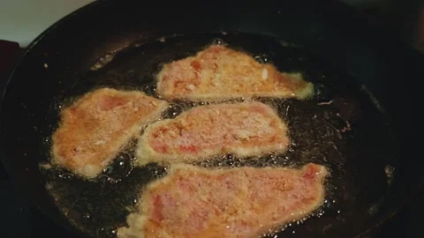 Hand adding breaded schnitzel to frying pan with sizzling schnitzels 23.976fps Video stock 311774581