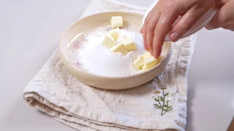 Hand adding butter cubes to a bowl of flour and sugar for baking on a kitch.. Video stock 346800019