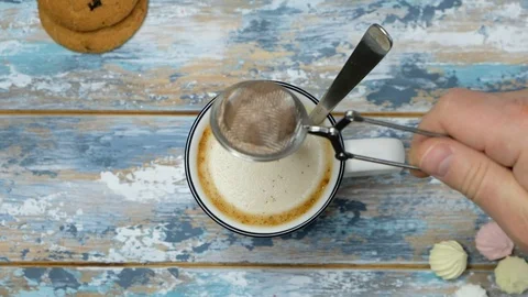 Hand adding cacao and stirring coffee cappuccino in a cup on wooden table, top Stock Footage 122495014