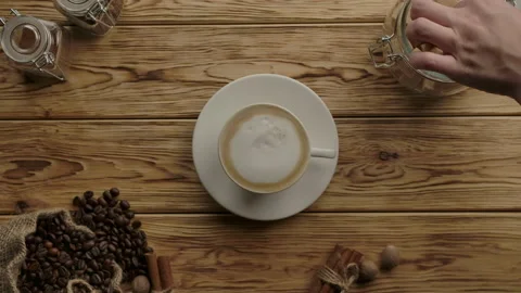 Hand adding cane brown sugar cubes and stirring with spoon into cappuccino Stock Footage 138523187