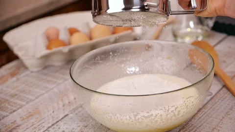 Hand adding flour to cake ingredients in glass bowl - using a sprinkler 動画素材 101863369