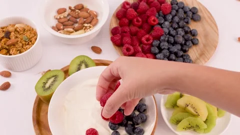 Hand Adding Fresh Raspberries to a Healthy Greek Yogurt Bowl Stock Footage 338321414