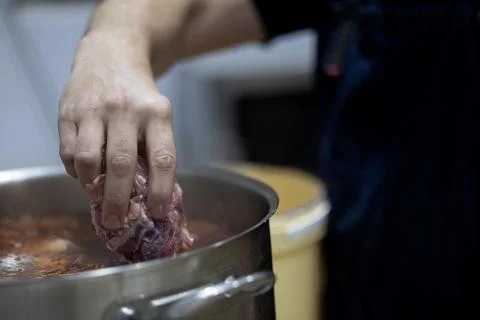 Hand adding fresh raw meat to boiling pot 스톡 사진