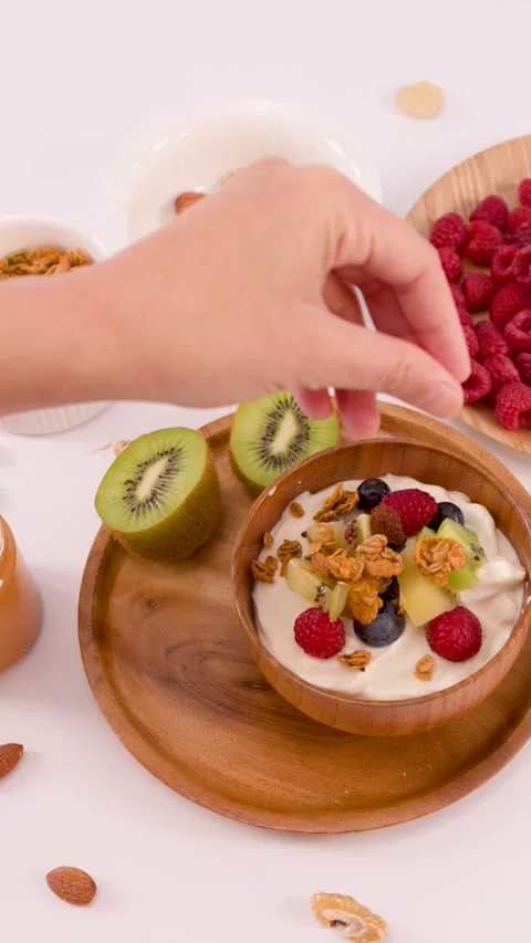 Hand Adding Granola and Nuts to Healthy Yogurt Fruit Bowl Stock Footage 337768907