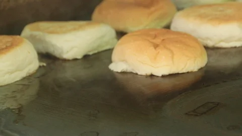 Hand adding hamburger buns on a smoking hot griddle Stock Footage 127716051