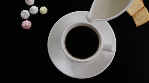 Hand adding milk to coffee and stirring coffee in a cup on black table, top view Stock Footage 122976103