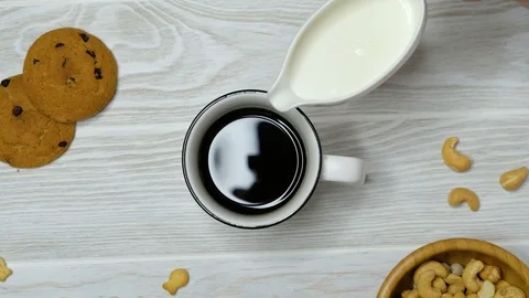 Hand adding milk to coffee in a cup on wooden table, top view Stock Footage 122494993