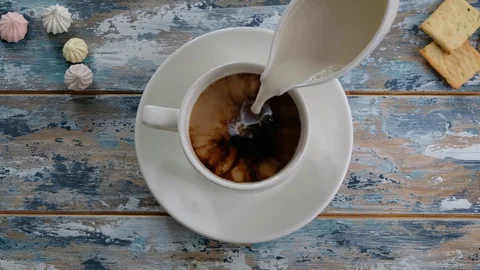 Hand adding milk to coffee in a cup on wooden table, top view Stock Footage 122906581