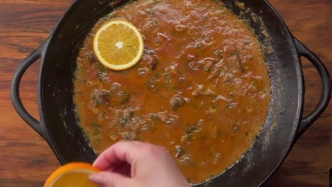 Hand Adding Orange Slices to Creamy Beef Stew in Wok Stock Footage 311060549