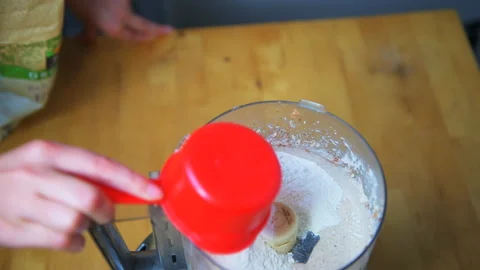 Hand adding organic wheat flour to peanut butter coconut oil in food processor Stock Footage 145564355