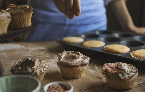Hand adding sprinkles to chocolate cupcake food photography recipe idea Stock Photos