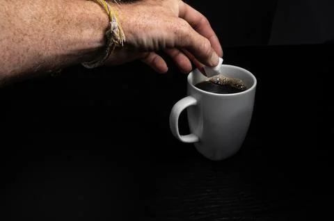 Hand Adding Sugar Cube to Coffee Mug Foto stock