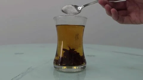 Hand adding sugar to a glass of black tea with tea leaves Stock Footage 284043362