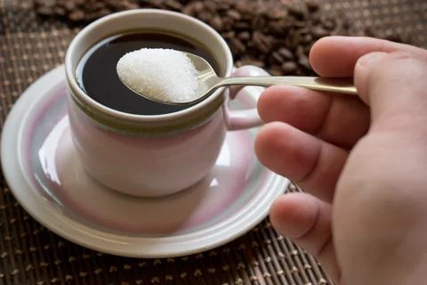 Hand adding sugar with spoon over a cup of coffee Stock Photos