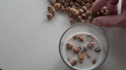 Hand Adding Tiger Nuts to Bowl of Liquid on White Table, Overhead Close Up Stock Footage 336477638