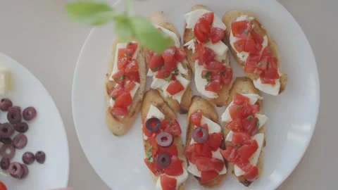 Hand adds black olive slices to bruschetta with tomato and mozzarella Stock Footage 337139143