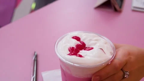 Hand adds cherry atop whipped cream, chocolate syrup, and sprinkles on pink Stock Footage 326625504