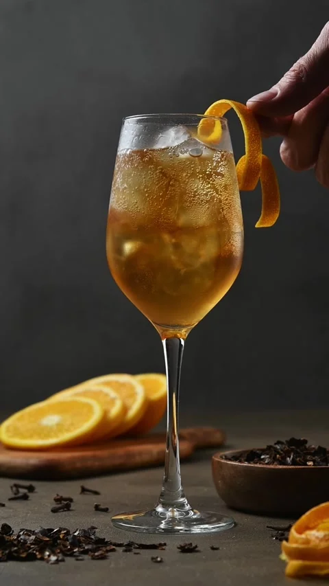 Hand adds curled orange peel garnish to iced spiced cascara spritz in stemmed Stockbeeldmateriaal 346265293