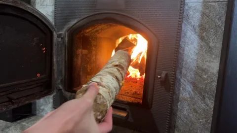 Hand adds firewood log into burning stove, cozy home heating concept Stock Footage 322671638