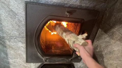 Hand adds firewood log into burning stove, cozy home heating concept Stock Footage 322671804