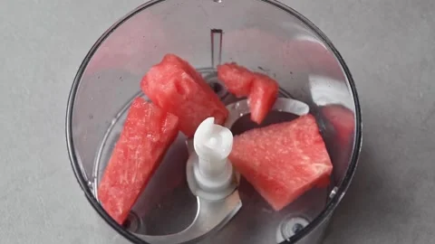 Hand adds fresh watermelon chunks to food processor bowl before blending Stock Footage 345793187