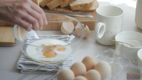 Hand adds salt to egg mixture in bowl before whisking, with bread slices nearby Stock Footage 339470423