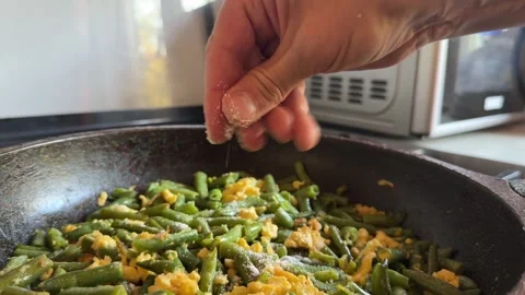 A hand adds salt to a pan with sautéed green beans. Simple moment of seasoning a Stock Footage 336524053