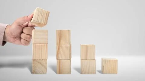 A hand adds a wooden cube to a stack of blocks arranged like a bar chart. P.. Foto stock