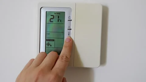 Hand adjusting a digital thermostat set to 22 degrees on a modern wall mounted Stock Footage 345653011