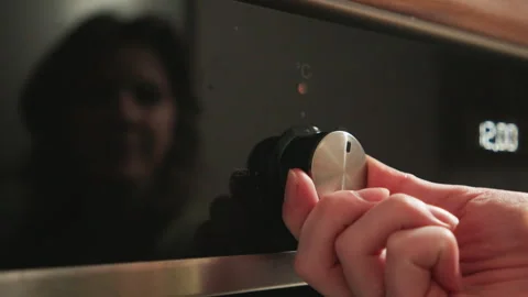 Hand adjusting metallic oven control knob on glossy black appliance with Stock-Footage 343540024