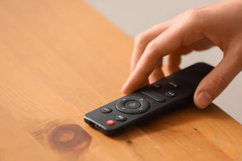 Hand adjusting smart home lighting remote control on wooden table, modern tec Stock Photos