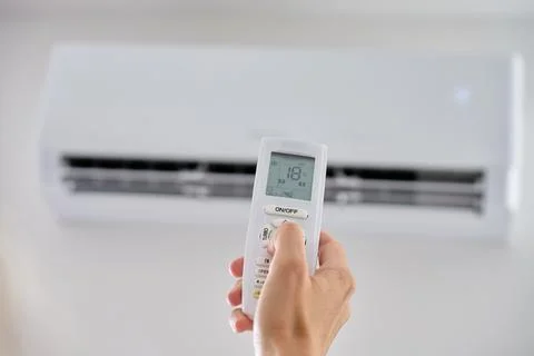Hand adjusting temperature on air conditioner with remote control Stock Photos