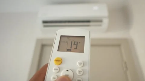 Hand adjusts air conditioner temperature down using remote control. Stock Footage 332777476
