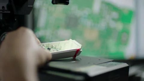 Hand Adjusts Small Electronic Device Under Microscope with Circuit Board Visible Stock Footage 334053679