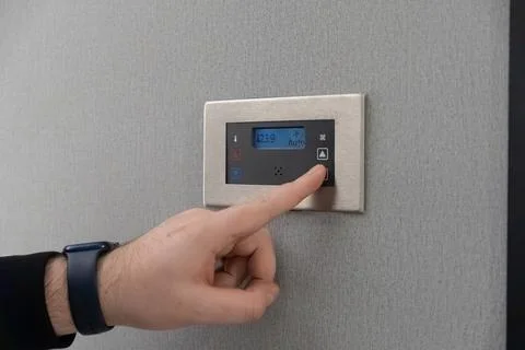A hand adjusts the temperature on a sleek wall mounted digital thermostat Stock Photos
