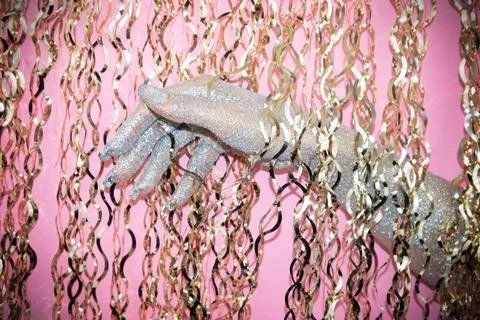 Hand adorned with glitter reaches through a cascade of shiny chains. Stock Photos